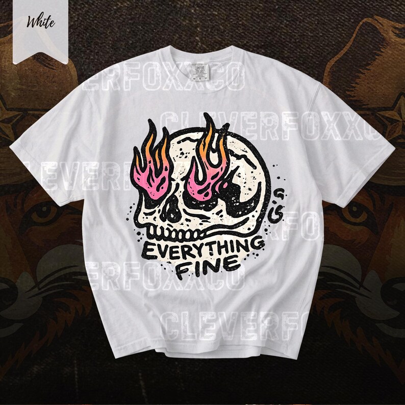 Puede incluir: Camiseta blanca con un dise&ntilde;o de calavera y llamas rosas y naranjas. El texto "EVERYTHING FINE" est&aacute; debajo de la calavera. La camiseta tiene mangas cortas y cuello redondo.