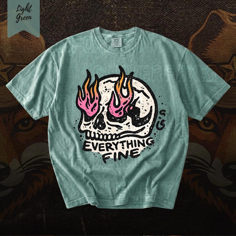 Puede incluir: Camiseta verde claro con un gr&aacute;fico de calavera y llamas rosas y naranjas. El texto "EVERYTHING FINE" est&aacute; debajo de la calavera. La camiseta es de color verde claro.
