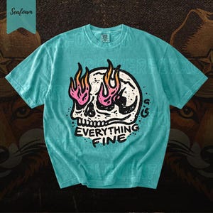 Puede incluir: Camiseta verde mar con un gr&aacute;fico de calavera y llamas rosas y naranjas. El texto "EVERYTHING FINE" est&aacute; debajo de la calavera. La camiseta tiene cuello redondo y mangas cortas.