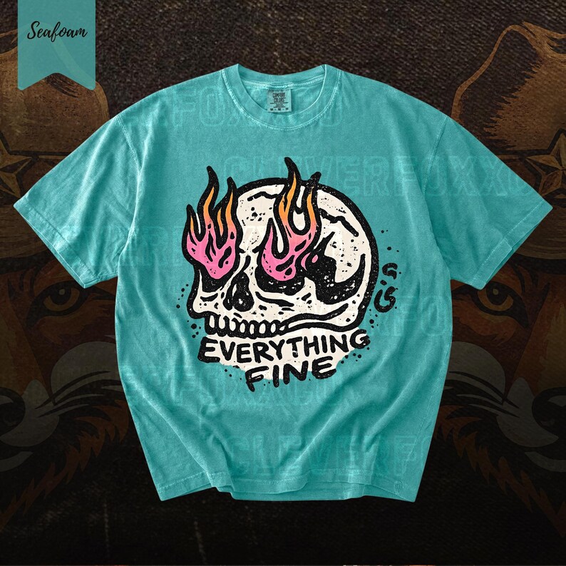 Puede incluir: Camiseta verde mar con un gr&aacute;fico de calavera y llamas rosas y naranjas. El texto "EVERYTHING FINE" est&aacute; debajo de la calavera. La camiseta tiene cuello redondo y mangas cortas.