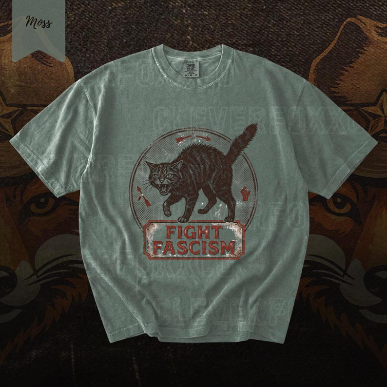 A gray t-shirt with a graphic design featuring a cat and the text "FIGHT FASCISM" printed on it.