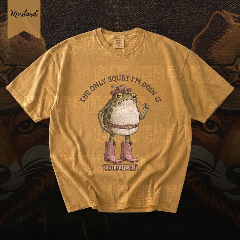 A yellow t-shirt with a cartoon frog wearing a cowboy hat and boots, along with the text "The only squat I'm done is I didlyy" printed on it.