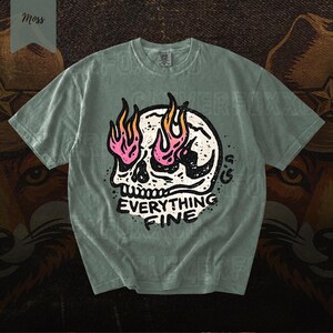 Puede incluir: Camiseta verde salvia con un dise&ntilde;o de calavera con llamas rosas y naranjas. El texto "EVERYTHING FINE" est&aacute; debajo. Cuello redondo, mangas cortas. La camiseta es de corte holgado.