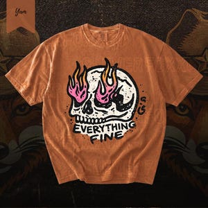 Puede incluir: Camiseta naranja con un dise&ntilde;o de calavera blanca con llamas rosas y amarillas. El texto "EVERYTHING FINE" est&aacute; impreso debajo. La camiseta tiene un aspecto vintage.