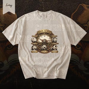 May include: An ivory short-sleeve t-shirt featuring a graphic of a circular clock-style pain scale. The design includes five opossums with varying facial expressions, Roman numerals, and text labels ranging from No Pain to Worst Pain Possible.