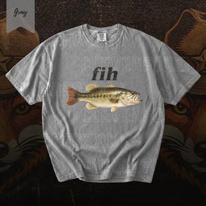 May include: Gray t-shirt featuring a detailed illustration of a fish with a red tail and yellow fins. The word "fih" is printed above the fish. The word "Gray" is in a banner in the upper left corner.