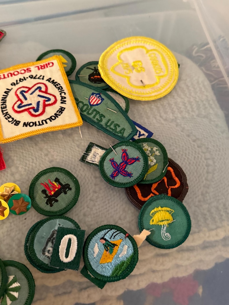 Op de afbeelding: Een verzameling Girl Scout en Boy Scout patches. De patches hebben verschillende ontwerpen, waaronder een rood, wit en blauw sterrenstelsel, een kampvuur en een ski&euml;r. De patches zijn in verschillende vormen en maten, met een mix van kleuren.