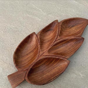 Puede incluir: Bandeja de servicio de madera con forma de hoja, hecha de madera marrón oscura. La bandeja tiene varios compartimentos, ideal para servir aperitivos o entremeses. El diseño de hoja añade un toque natural y elegante a cualquier mesa.
