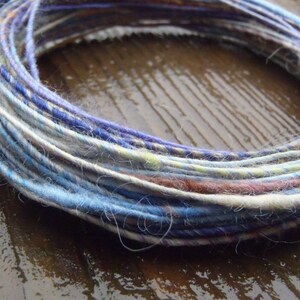 Puede incluir: Un ovillo de hilo en tonos de azul, blanco y marrón. El hilo está enrollado en un círculo y tiene una textura peluda.