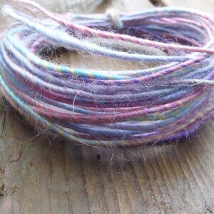 May include: A close-up of a skein of yarn in shades of purple, pink, and blue. The yarn is made of a soft, fuzzy material and is perfect for knitting or crocheting.