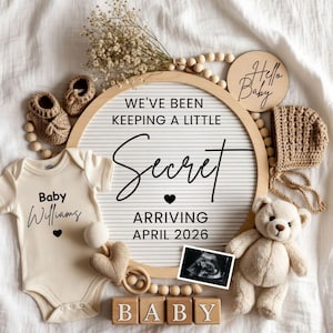 Può includere: Annuncio nascita dai toni neutri con il testo "We've been keeping a little secret" e "Arriving April 2026". Include un body, un orsacchiotto, scarpine e blocchi di legno con la parola "BABY".
