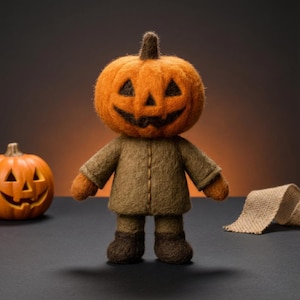 Könnte beinhalten: Eine handgefertigte Filzfigur mit Kürbiskopf, braunem Mantel und Stiefeln, ideal für Halloween-Dekorationen. Die Figur hat ein geschnitztes Gesicht mit dreieckigen Augen und einem lächelnden Mund. Ein oranger Kürbis und ein Jutegewebe sind ebenfalls im Bild.