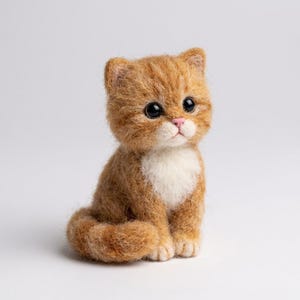 May include: A needle-felted ginger tabby kitten figurine with a white chest and muzzle. The small cat has large, round, black eyes, a tiny pink nose, and a textured, fuzzy appearance. It is sitting in an upright position with its tail curled.