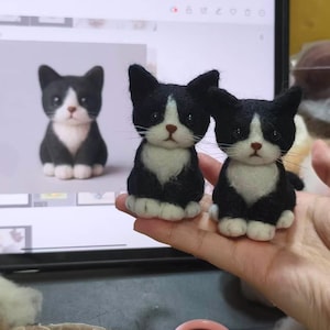May include: Two small, handcrafted needle-felted cat figurines featuring black and white fur, pointed ears, dark eyes, and a small brown nose. The cats are depicted in a sitting position with white paws and a white chest patch, mirroring the digital image.