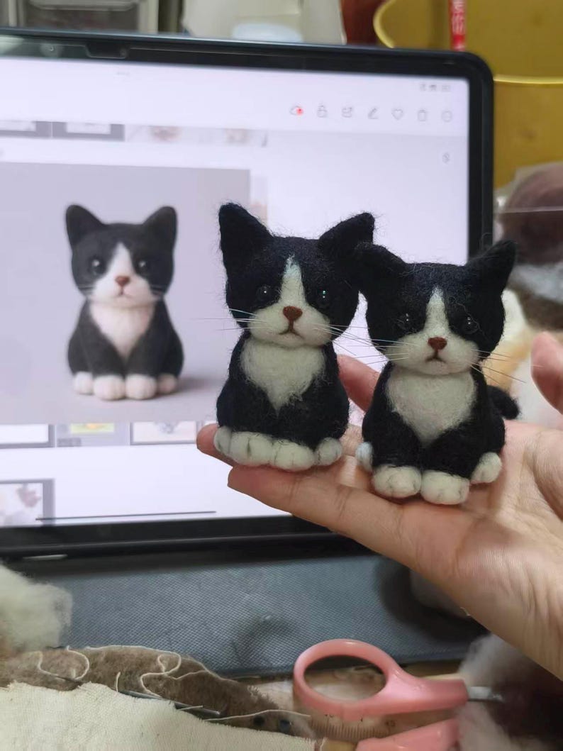 May include: Two small, handcrafted needle-felted cat figurines featuring black and white fur, pointed ears, dark eyes, and a small brown nose. The cats are depicted in a sitting position with white paws and a white chest patch, mirroring the digital image.