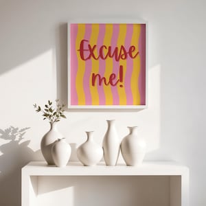 May include: A framed artwork with the text "Excuse me!" in red script against a background of pink and yellow vertical stripes. Below, a white shelf displays five white ceramic vases, some holding greenery.