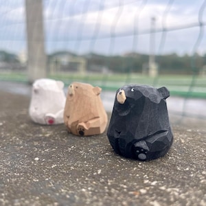 Op de afbeelding: Drie houten berenbeeldjes in wit, bruin en zwart. De beren zitten met hun poten zichtbaar. De zwarte beer heeft een lichtgekleurde snuit en oren. De witte beer heeft een rood geschilderde onderkant.