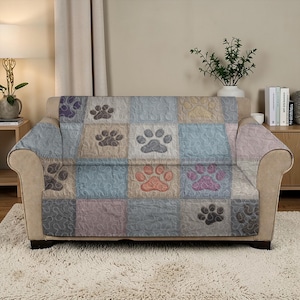 May include: A patchwork sofa cover featuring paw prints in various colors, including purple, orange, and gray. The cover is quilted and designed to fit over a two-seater sofa, offering a decorative and protective layer.