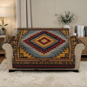 May include: A beige sofa with a colorful, patterned quilt draped over it. The quilt features a central diamond design in red, yellow, and blue, with geometric borders. The sofa is in a well-lit room with a neutral color palette.