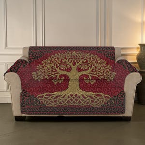 May include: A red sofa cover featuring a gold tree of life motif. The tree design has detailed roots and branches, with a decorative border. The cover is draped over a beige sofa, adding a decorative element to the furniture.