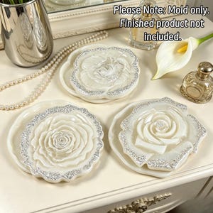 May include: Three circular silicone molds featuring a raised rose design with scalloped edges. The molds are white with silver glitter accents along the borders. Text on the image reads: Please Note: Mold only. Finished product not included.