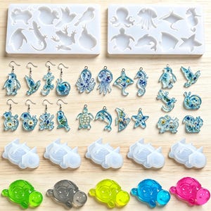 May include: Two rectangular silicone molds with animal shapes, a collection of resin charms and earrings featuring embedded blue flowers, and five translucent turtle-shaped resin figures in green, gray, yellow, blue, and pink colors.