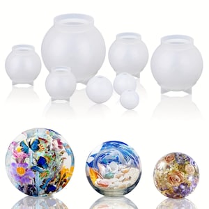 May include: A collection of clear, spherical resin molds in various sizes, alongside three decorative glass spheres. The spheres feature colorful floral, ocean, and dried flower designs, perfect for crafting or home decor.
