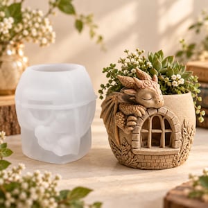 May include: A translucent silicone mold for a planter next to a finished beige resin planter featuring a sculpted sleeping dragon resting on a brick-textured wall with an arched window, containing a small green succulent plant with tiny white flowers.