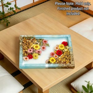 May include: A rectangular silicone mold for a tray featuring a light blue border with gold leaf accents. The interior surface is white and contains embedded dried flowers in shades of yellow, pink, and red. Text reads: Please Note: Mold only. Finished product not included.