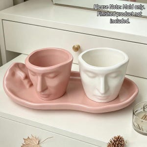 May include: A pink and white silicone mold set featuring two face-shaped planters on an oval tray. The text on the image reads: Please Note: Mold only. Finished product not included. The molds have detailed facial features including eyes, noses, and lips.