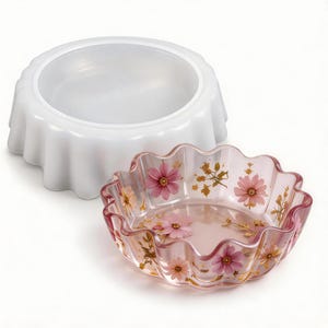 May include: A translucent white silicone mold with a fluted edge and a matching clear resin bowl featuring embedded pink cosmos flowers and delicate gold leaf accents, showcasing a scalloped rim and a smooth, glossy finish on the interior.