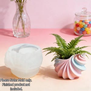 May include: A translucent white silicone mold shaped like a spiral seashell alongside a finished ceramic seashell planter containing a green fern. The text on the image reads: Please Note: Mold only. Finished product not included.