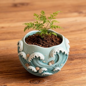 May include: A light blue ceramic planter with a wave design, seashells, and a small plant. The planter is filled with soil and has a round shape. The wave design is white and blue.