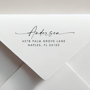 May include: A white envelope featuring black printed text on the flap. The text displays the name Andersen in a cursive script font, followed by the address 4278 Palm Grove Lane, Naples, FL 34102 in a clean, sans-serif capital letter typeface.