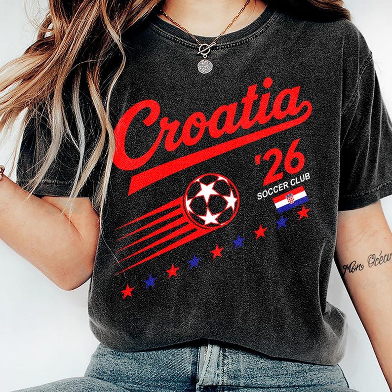 May include: A charcoal grey short-sleeve t-shirt featuring the red text Croatia, the number 26, and the words SOCCER CLUB. The design includes a graphic of a soccer ball with motion lines, a small Croatian flag, and a row of red and blue stars.
