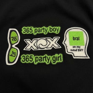 Puede incluir: Una sudadera negra con parches bordados en verde lima, blanco y negro. El diseño incluye el texto 365 party boy, 365 party girl, XCX y brat, junto con gráficos de gafas de sol y una silueta de cabeza humana con texto.