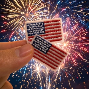 May include: Two rectangular embroidered patches featuring the United States flag design. Each patch displays a blue canton with white stars and alternating red and white horizontal stripes, rendered in detailed thread work with a white border.