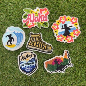 Puede incluir: Seis parches bordados con varios diseños: un letrero rosa de Aloha con flores, una bailarina de hula enmarcada por hibiscos, un surfista en una ola azul, una bota de senderismo amarilla con el texto Take a Hike, un escudo de Rafting Adventure y un mapa de EE. UU.