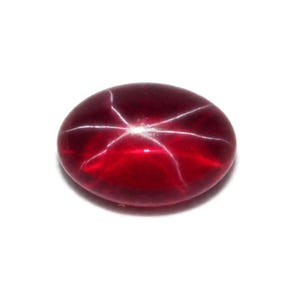 Puede incluir: Una gema pulida, de forma ovalada, de color rojo intenso, con un patrón de estrella de seis rayos. El efecto de estrella se crea por la luz que se refleja en las inclusiones dentro de la piedra. La gema está sobre un fondo blanco.
