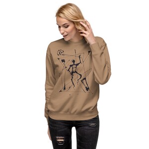 May include: A tan sweatshirt featuring a black abstract design of a figure within geometric shapes. The long-sleeved crew neck top is made of a soft material. The design is a unique artistic statement.