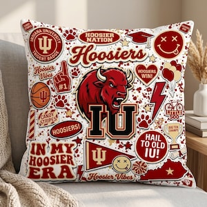 Puede incluir: Coj&iacute;n cuadrado blanco con gr&aacute;ficos rojos y negros. Incluye textos como "Hoosiers" e "IU", junto con un bisonte rojo, huellas de patas y una pelota de baloncesto.