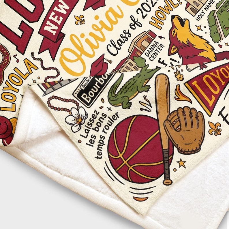 Puede incluir: Manta color crema con un dise&ntilde;o burdeos y dorado. Presenta el nombre "Olivia", "Class of 2023" e ilustraciones que incluyen un lobo, un caim&aacute;n, b&eacute;isbol y baloncesto. Incluye el texto "Laissez les bons temps rouler".