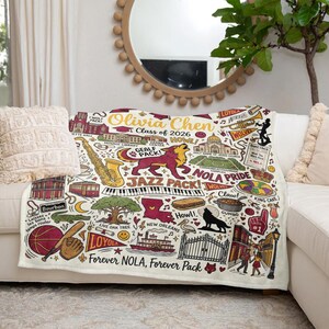 Puede incluir: Una manta crema con un dise&ntilde;o colorido con tem&aacute;tica de Nueva Orleans. La manta incluye ilustraciones de un saxof&oacute;n, teclas de piano de jazz, un le&oacute;n y el texto "Forever NOLA, Forever Pack".