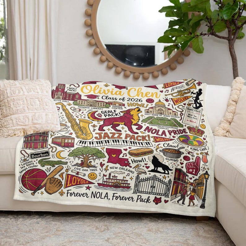 Puede incluir: Una manta crema con un dise&ntilde;o colorido con tem&aacute;tica de Nueva Orleans. La manta incluye ilustraciones de un saxof&oacute;n, teclas de piano de jazz, un le&oacute;n y el texto "Forever NOLA, Forever Pack".