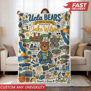 Puede incluir: Una manta color crema con un dise&ntilde;o colorido con el texto "UCLA BEARS" y "Jake Wilson". El dise&ntilde;o incluye ilustraciones de monumentos, una mascota de oso y el texto "Class of 2026". La manta tiene una pancarta roja "FAST DELIVERY".