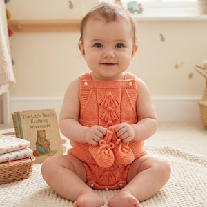Peut inclure: Un bébé souriant porte un barboteuse tricotée orange et des chaussons assortis. La barboteuse présente un motif texturé avec des perles. Le bébé tient les chaussons et est assis sur un tapis crème. Un livre intitulé "The Little Bear's Knitting Adventure" est visible.