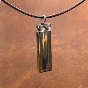 May include: A rectangular pendant necklace with a dark brown leather cord. The pendant is a dark, marbled stone wrapped with copper wire. The stone has shades of brown, tan, and black. The pendant is approximately 2 inches long.