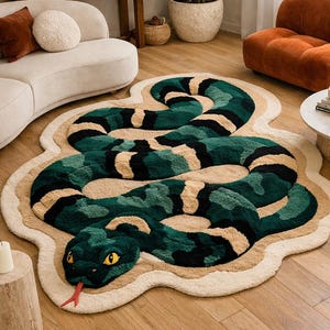 Puede incluir: Una alfombra decorativa con forma de serpiente, en tonos verdes y negros, con detalles beige. La alfombra presenta una cabeza de serpiente detallada con ojos amarillos y una lengua roja. Está colocada sobre un suelo de madera.
