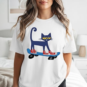May include: White t-shirt featuring a navy blue cat with yellow eyes and red sneakers skateboarding on a blue skateboard. The cat has a curved tail. The design is a cartoon illustration.