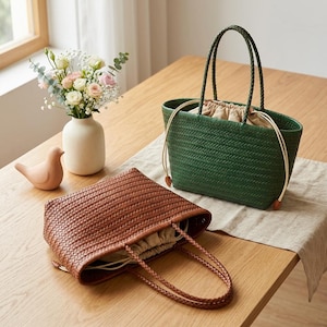 Peut inclure: Deux sacs cabas tressés, l'un vert foncé et l'autre marron, dotés chacun d'une anse tressée et d'une doublure en tissu beige à cordon de serrage. Les sacs présentent un motif en chevrons et sont accompagnés d'une figurine d'oiseau en céramique.